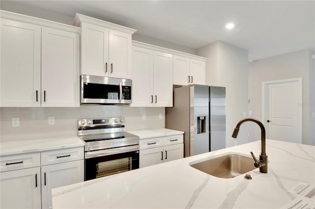 kitchen featuring decorative backsplash, light stone countertops, white cabinetry, a sink, and appliances with stainless steel finishes