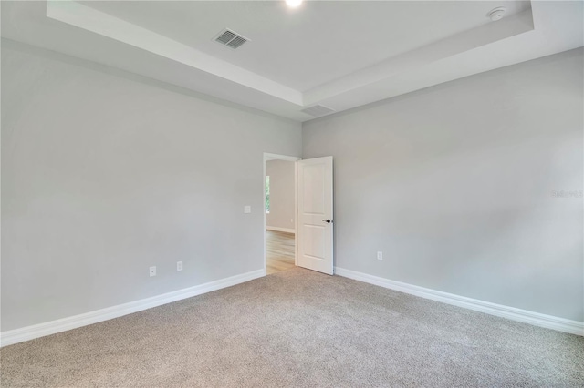 unfurnished room with visible vents, a raised ceiling, baseboards, and light carpet