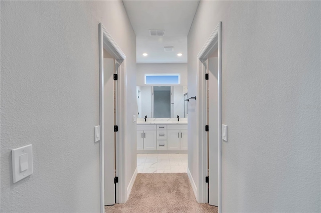 corridor with a textured wall, light carpet, a sink, baseboards, and visible vents