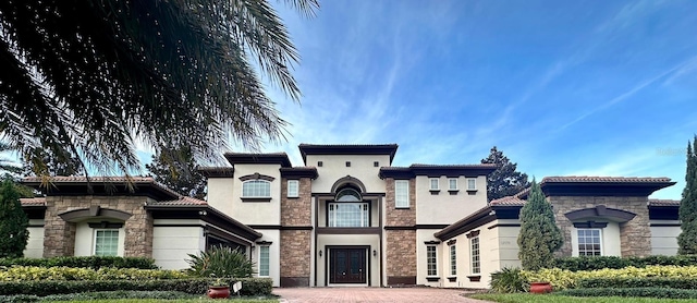 mediterranean / spanish home featuring decorative driveway, stucco siding, a tiled roof, and stone siding