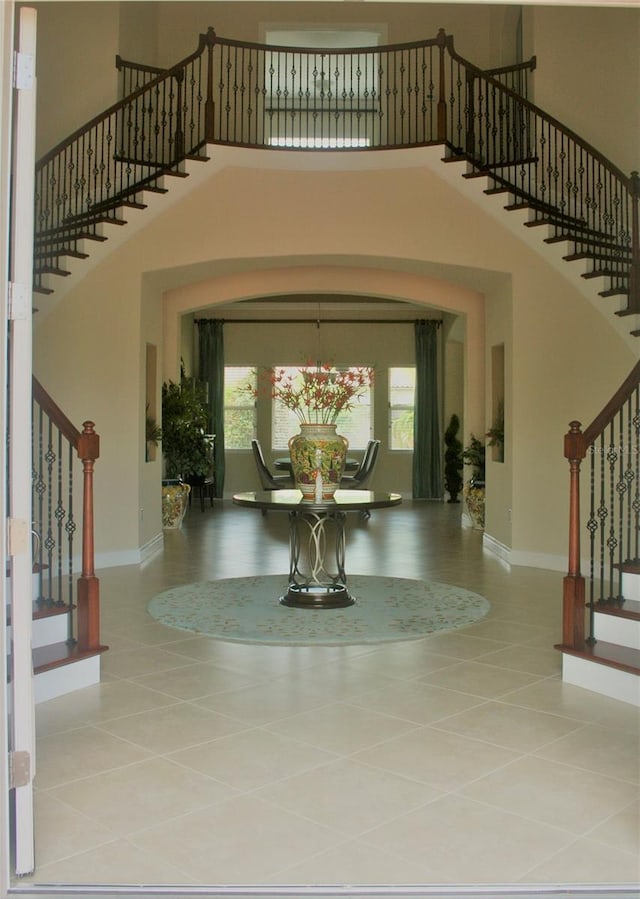 tiled entrance foyer featuring baseboards, a high ceiling, stairway, and an inviting chandelier