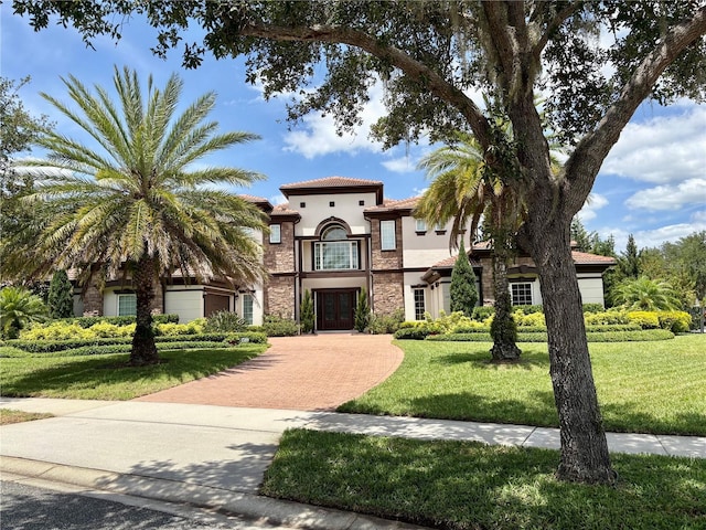 mediterranean / spanish house featuring a front lawn, stone siding, decorative driveway, stucco siding, and french doors