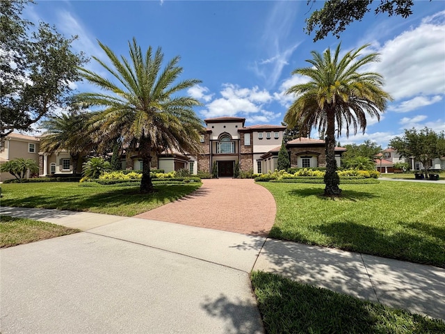 mediterranean / spanish-style home with stucco siding, a front lawn, decorative driveway, and stone siding