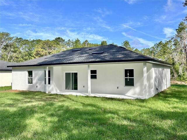 back of house featuring a yard, roof with shingles, and stucco siding