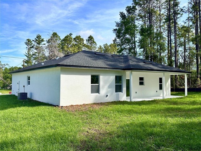 back of house featuring a lawn, central air condition unit, a patio area, and stucco siding