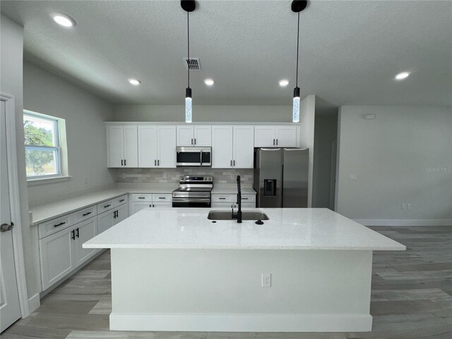 kitchen featuring visible vents, an island with sink, a sink, light wood finished floors, and stainless steel appliances