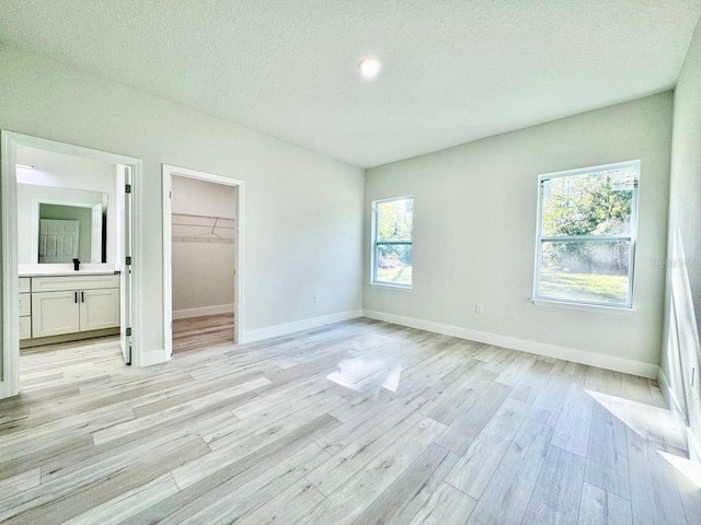 unfurnished bedroom with a closet, baseboards, a walk in closet, a textured ceiling, and light wood finished floors