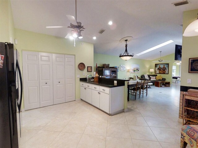 kitchen featuring vaulted ceiling with skylight, a ceiling fan, dark countertops, freestanding refrigerator, and a peninsula