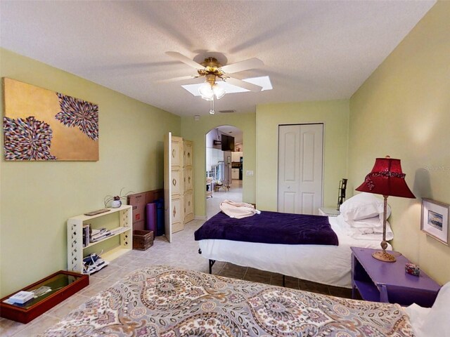 bedroom with ceiling fan, a textured ceiling, arched walkways, tile patterned floors, and a closet