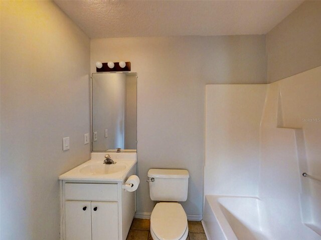 full bathroom with vanity, toilet, a tub, a textured ceiling, and tile patterned floors
