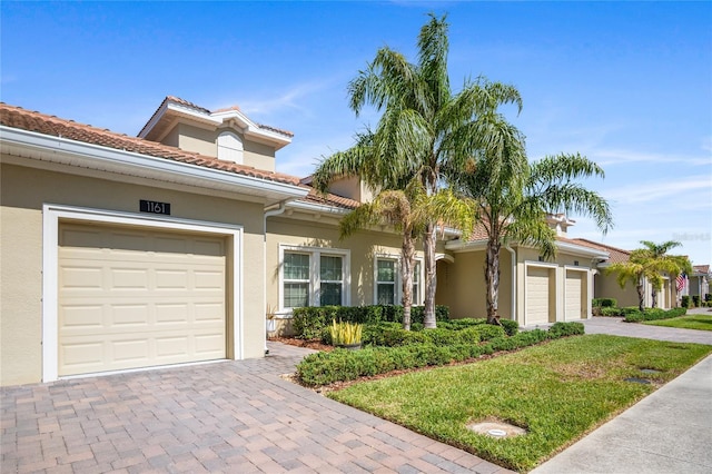 mediterranean / spanish-style house featuring a tiled roof, driveway, a garage, a front lawn, and stucco siding