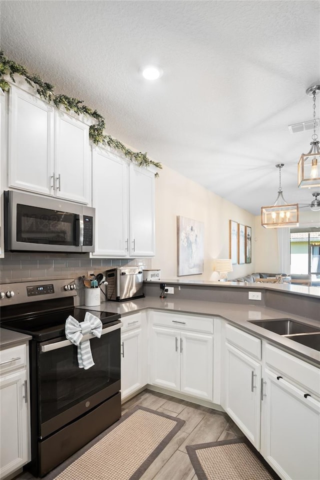 kitchen with light wood finished floors, a chandelier, stainless steel appliances, white cabinetry, and decorative backsplash