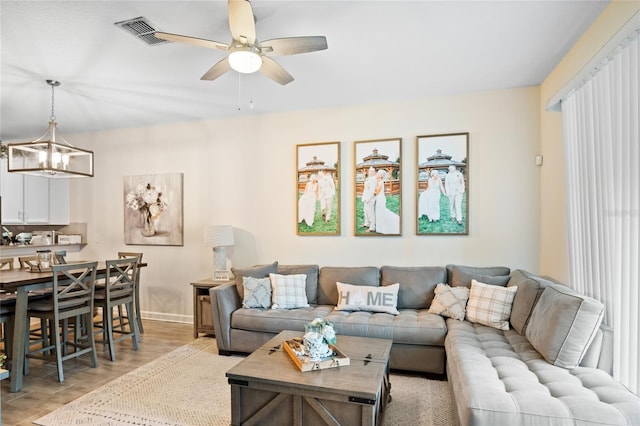 living room with light wood-style floors, baseboards, ceiling fan with notable chandelier, and visible vents