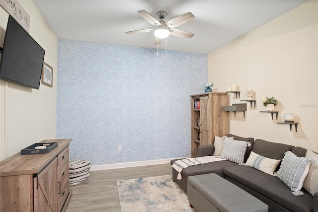 living area featuring baseboards, a ceiling fan, wallpapered walls, and light wood-style flooring