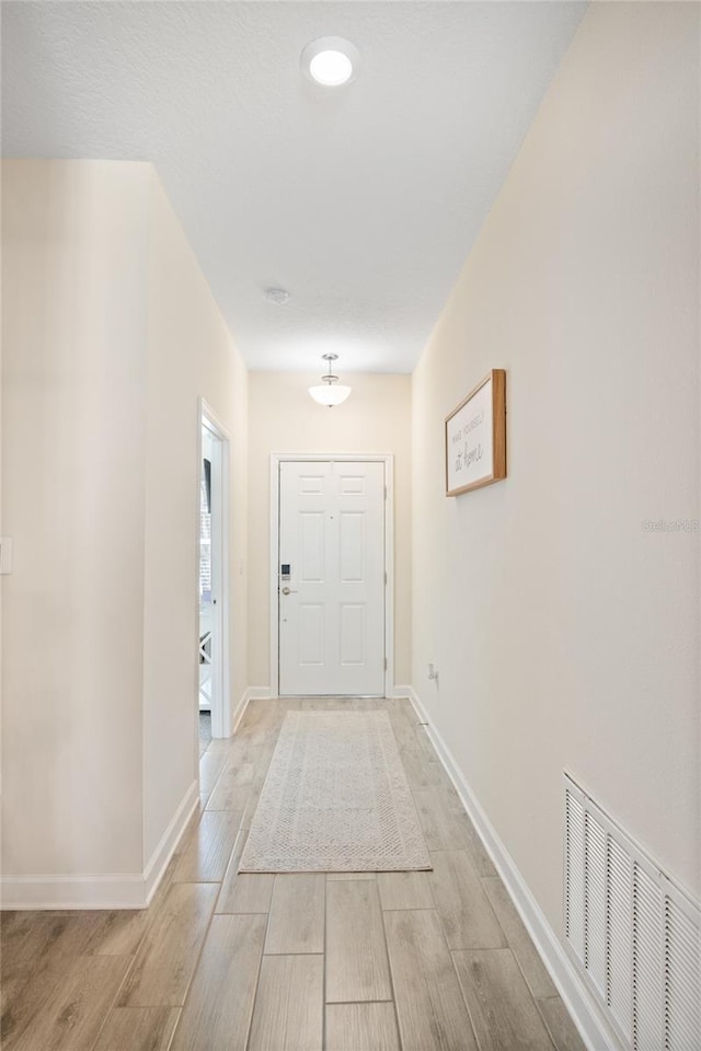 corridor with light wood-style floors, baseboards, and visible vents