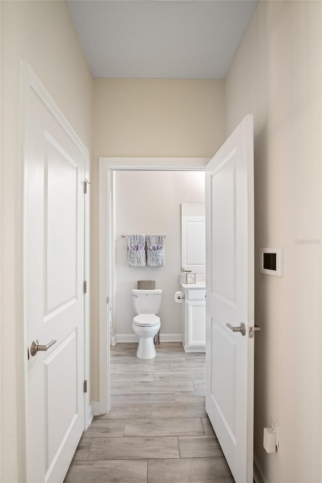 half bathroom with baseboards, wood finished floors, toilet, and vanity