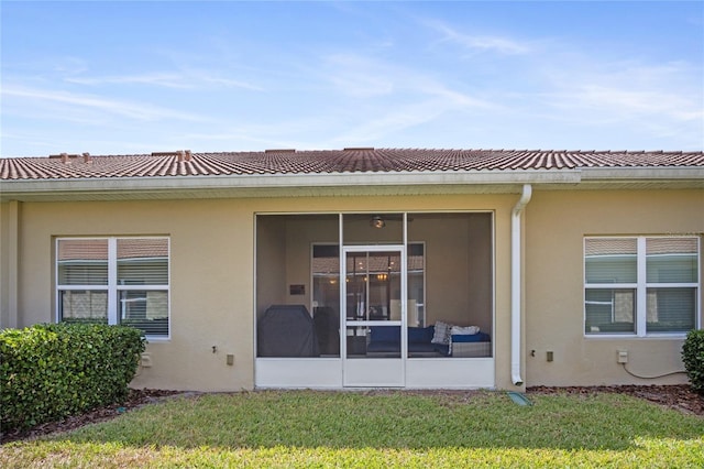 rear view of property with a sunroom, a lawn, and stucco siding