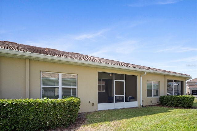 back of house with a sunroom, stucco siding, and a yard