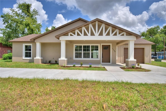 view of front of house featuring an attached garage, stucco siding, driveway, covered porch, and a front lawn