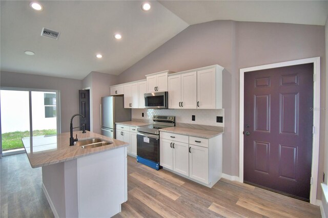 kitchen featuring appliances with stainless steel finishes, a sink, a kitchen island with sink, vaulted ceiling, and light wood-type flooring