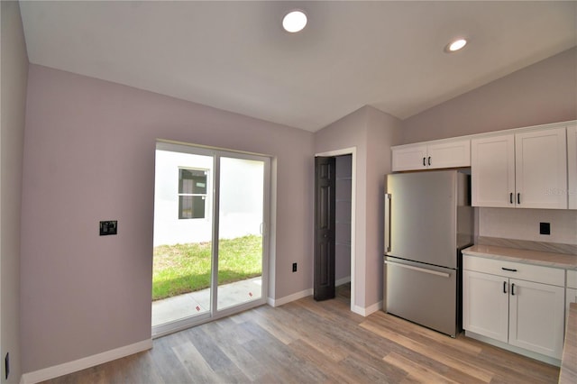 kitchen featuring freestanding refrigerator, baseboards, vaulted ceiling, white cabinetry, and light wood-style floors