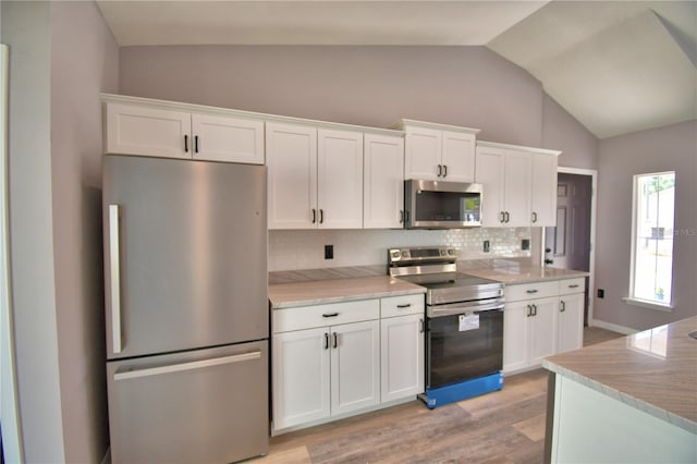 kitchen with stainless steel appliances, vaulted ceiling, white cabinets, tasteful backsplash, and light wood finished floors