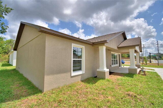 view of side of home featuring stucco siding, a lawn, and a shingled roof