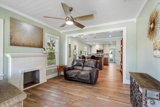 living room featuring baseboards, light wood-style flooring, ceiling fan, crown molding, and a brick fireplace
