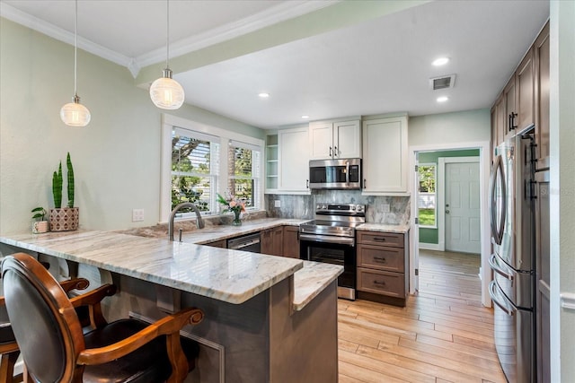kitchen with appliances with stainless steel finishes, a peninsula, crown molding, light stone counters, and light wood-type flooring