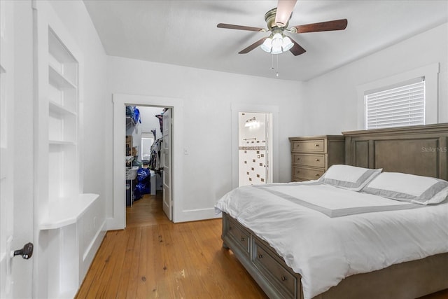 bedroom with a spacious closet, baseboards, a closet, light wood-type flooring, and a ceiling fan