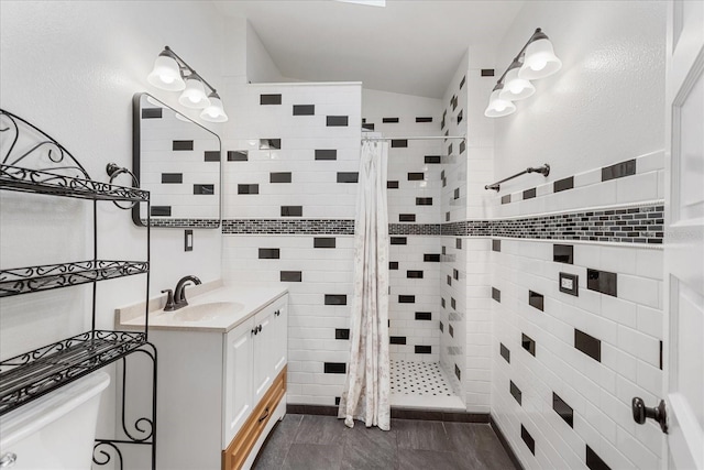 bathroom featuring a stall shower, toilet, vanity, tile walls, and vaulted ceiling