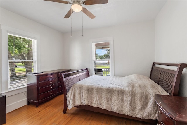 bedroom with light wood-type flooring, multiple windows, a ceiling fan, and baseboards