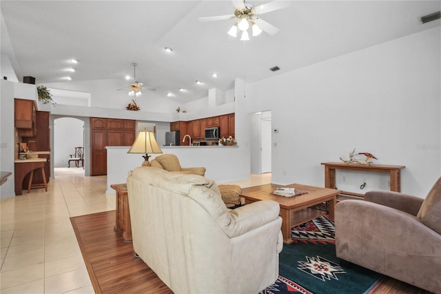living room with visible vents, ceiling fan, arched walkways, light tile patterned floors, and vaulted ceiling