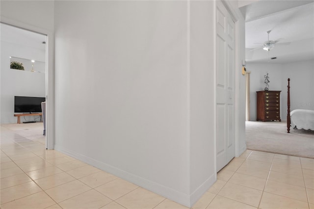 hall featuring light tile patterned floors, baseboards, and light colored carpet