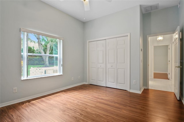 unfurnished bedroom with visible vents, a closet, wood finished floors, baseboards, and a ceiling fan