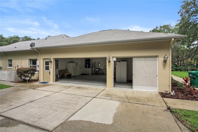 back of property with a garage, stucco siding, concrete driveway, and a shingled roof