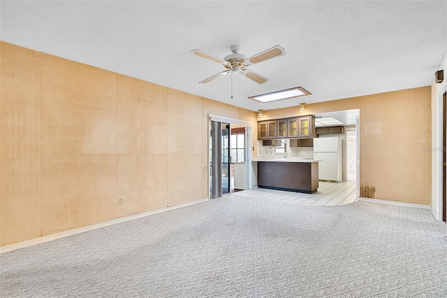 unfurnished living room with a ceiling fan, baseboards, and light carpet