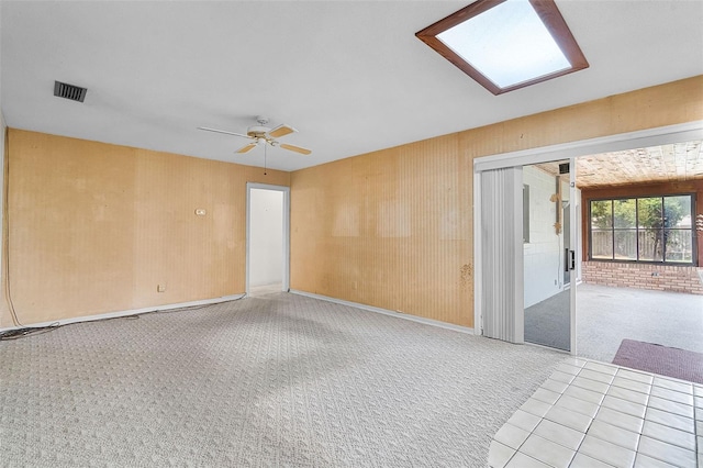 empty room featuring visible vents, a ceiling fan, a skylight, and light carpet