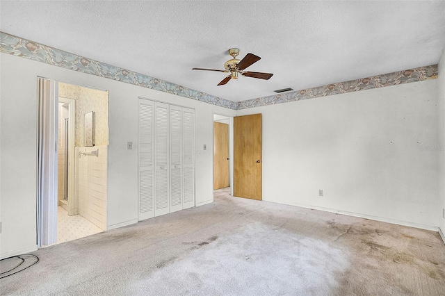 unfurnished bedroom featuring a textured ceiling, visible vents, carpet floors, a closet, and ensuite bath
