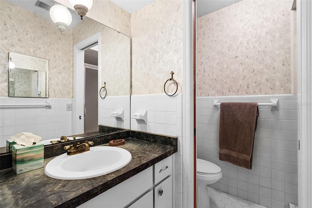 bathroom with vanity, toilet, tile patterned floors, a wainscoted wall, and tile walls
