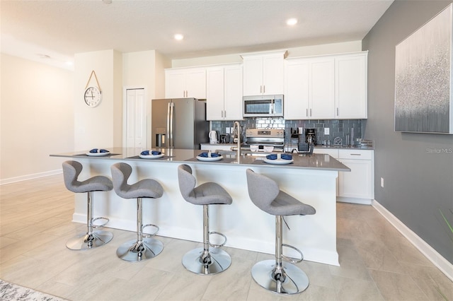 kitchen featuring a breakfast bar, an island with sink, stainless steel appliances, white cabinetry, and decorative backsplash