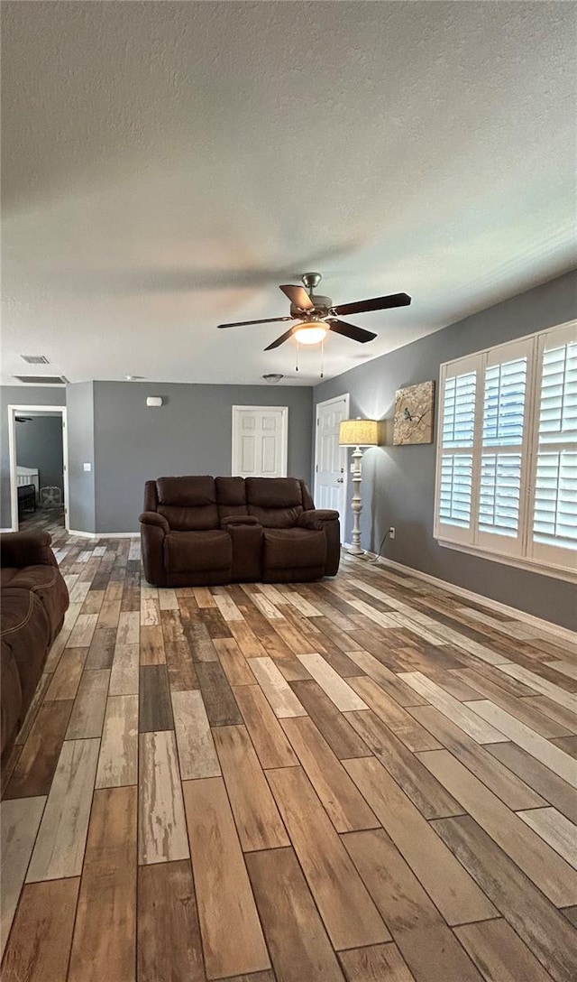 living room with a textured ceiling, baseboards, a ceiling fan, and hardwood / wood-style floors