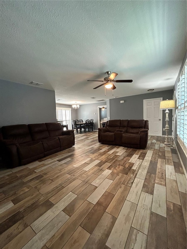 living area with a ceiling fan, a textured ceiling, visible vents, and wood finished floors
