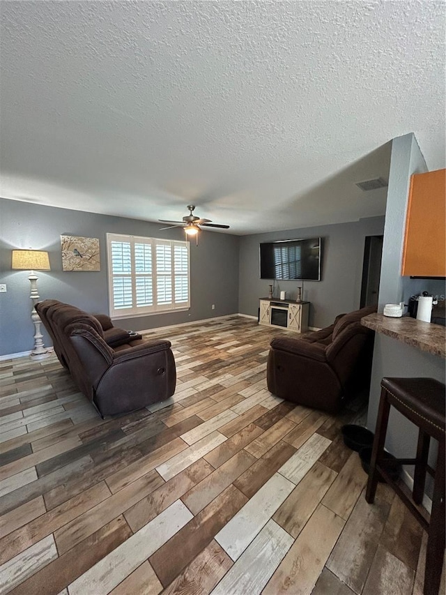 living area with visible vents, ceiling fan, a textured ceiling, and wood finished floors