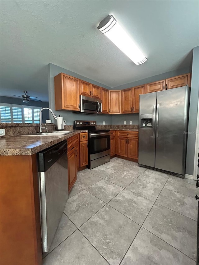 kitchen featuring dark countertops, brown cabinets, a sink, light tile patterned floors, and stainless steel appliances