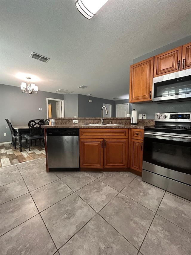 kitchen featuring visible vents, an inviting chandelier, brown cabinets, a sink, and stainless steel appliances