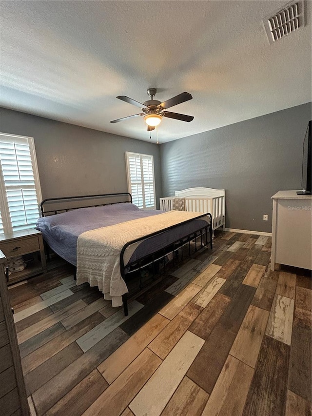 bedroom featuring ceiling fan, wood-type flooring, a textured ceiling, and visible vents