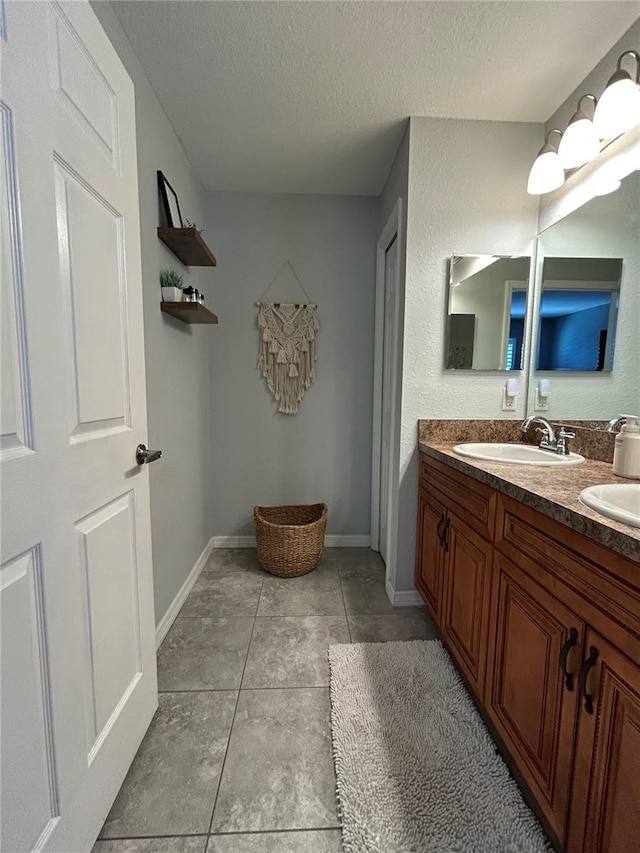 full bath with double vanity, a textured ceiling, tile patterned flooring, a sink, and baseboards