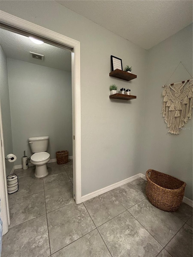 bathroom with toilet, tile patterned floors, a textured ceiling, baseboards, and visible vents