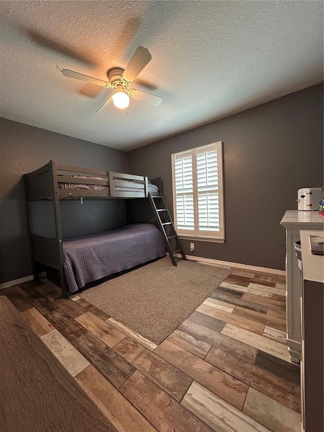 bedroom with baseboards, a textured ceiling, ceiling fan, and hardwood / wood-style floors